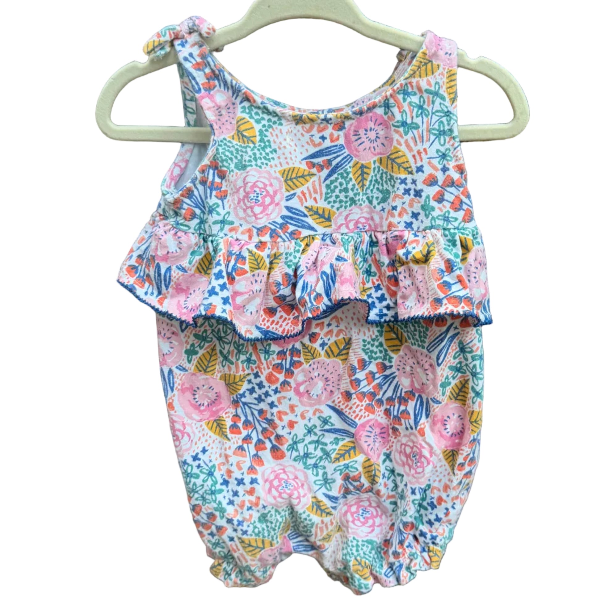 A sleeveless baby romper with a colorful floral print hangs on a white plastic hanger against a brick wall background.