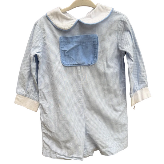 A light blue and white gingham baby romper with a solid light blue chest pocket and white collar, hanging on a wooden hanger against a brick wall.
