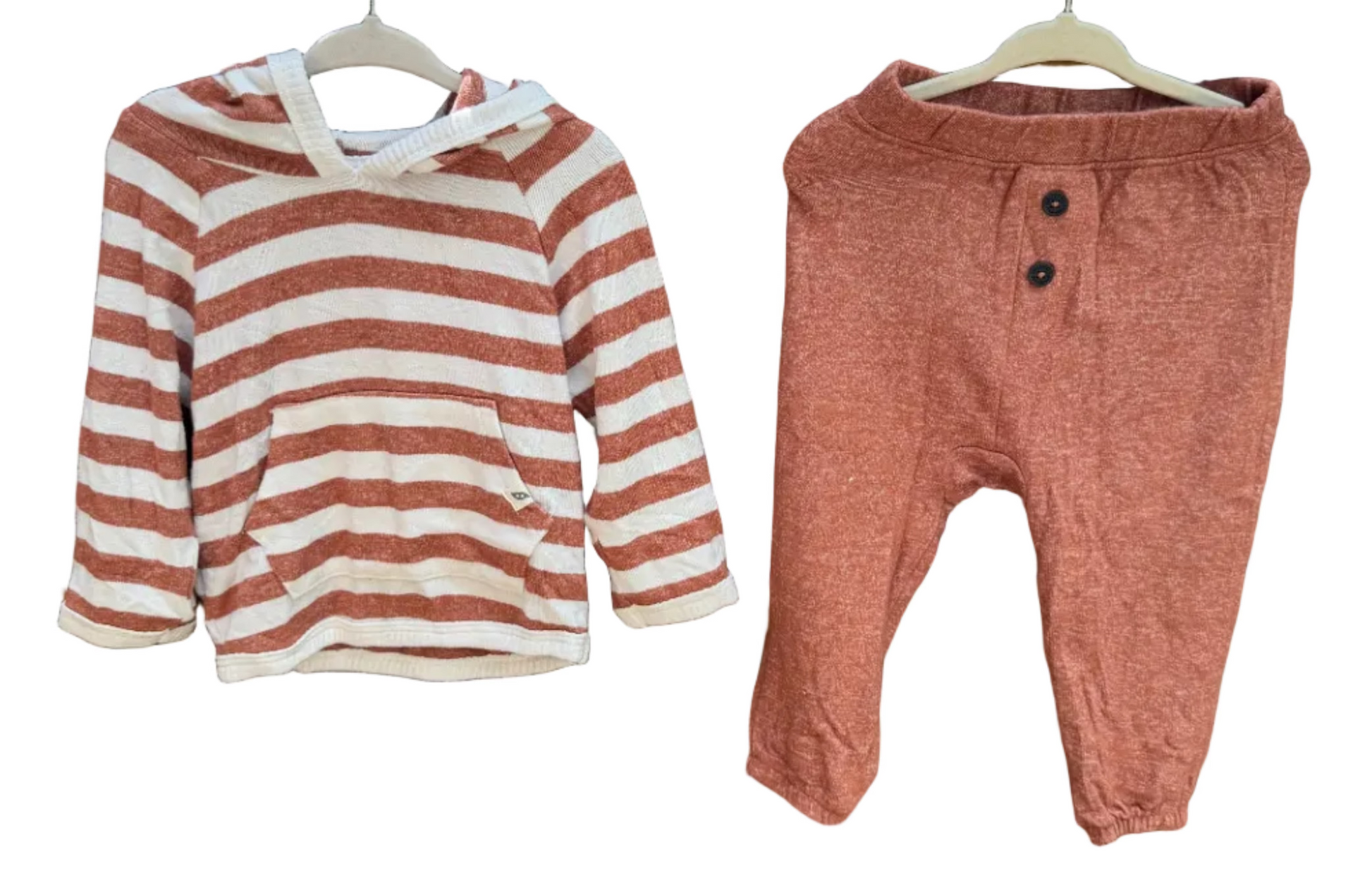 A toddler's two-piece clothing set hanging on a brick wall outdoors. The set includes a long-sleeve hooded shirt with horizontal terracotta and white stripes, and matching dusty rose pants with a three-button henley neckline.
