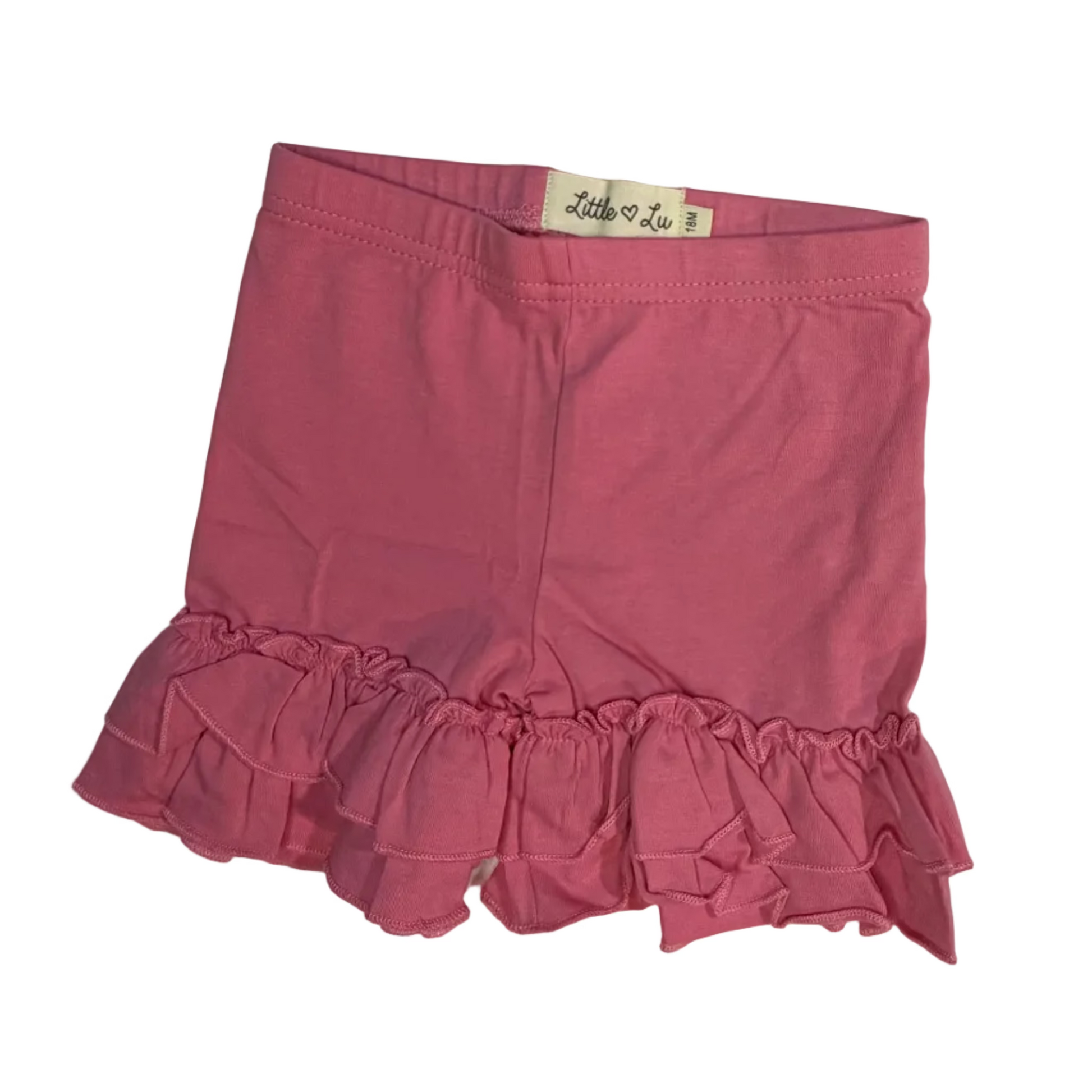 A pink ruffled mini skirt laid flat on a white sheet, with a small white brand label visible at the waistband.